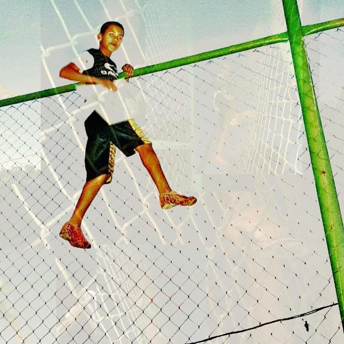 Menino equilibrado na trave verde do campo, céu claro ao fundo