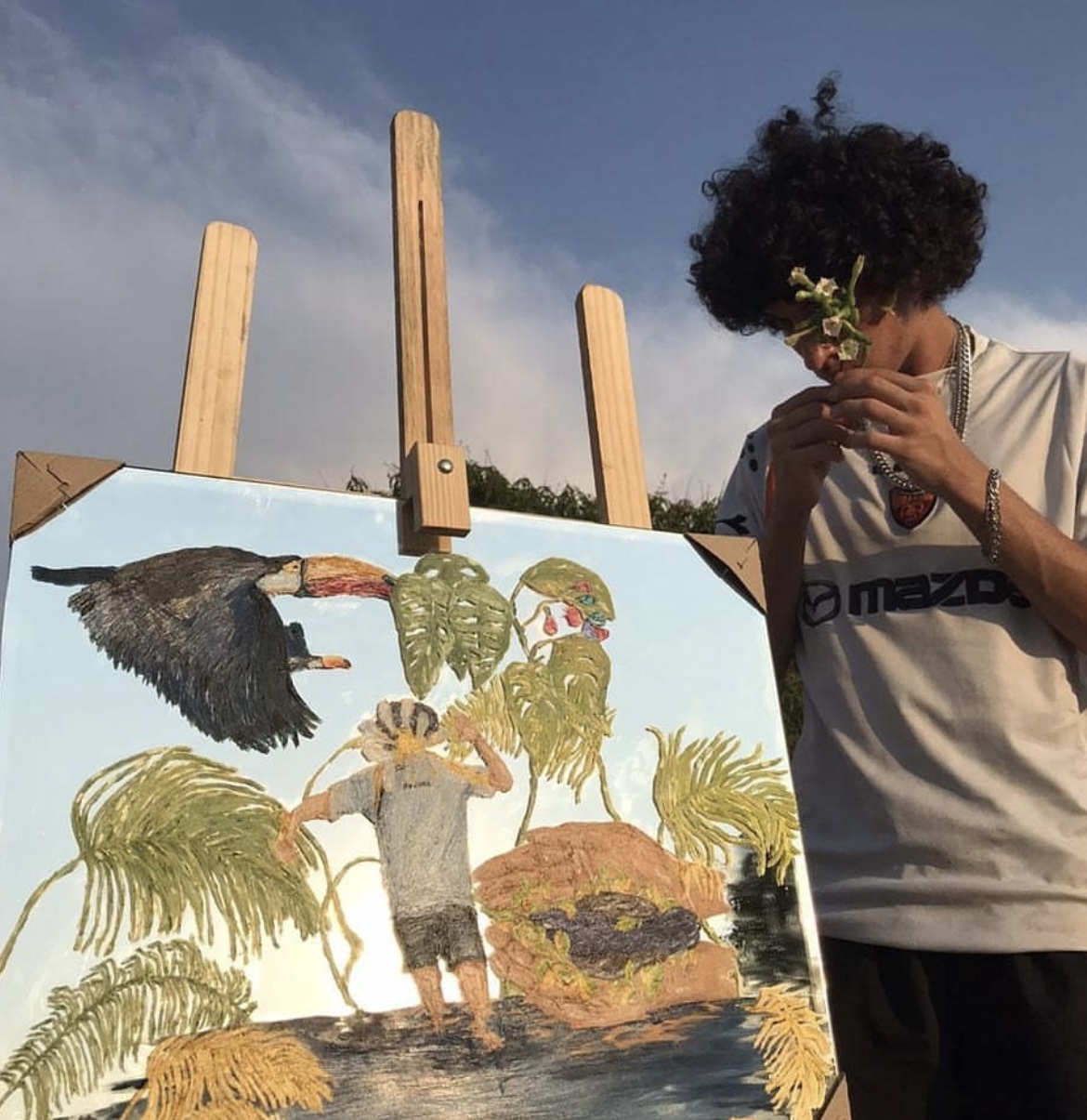 O artista segurando um ramo de flores ao lado do espelho pintado