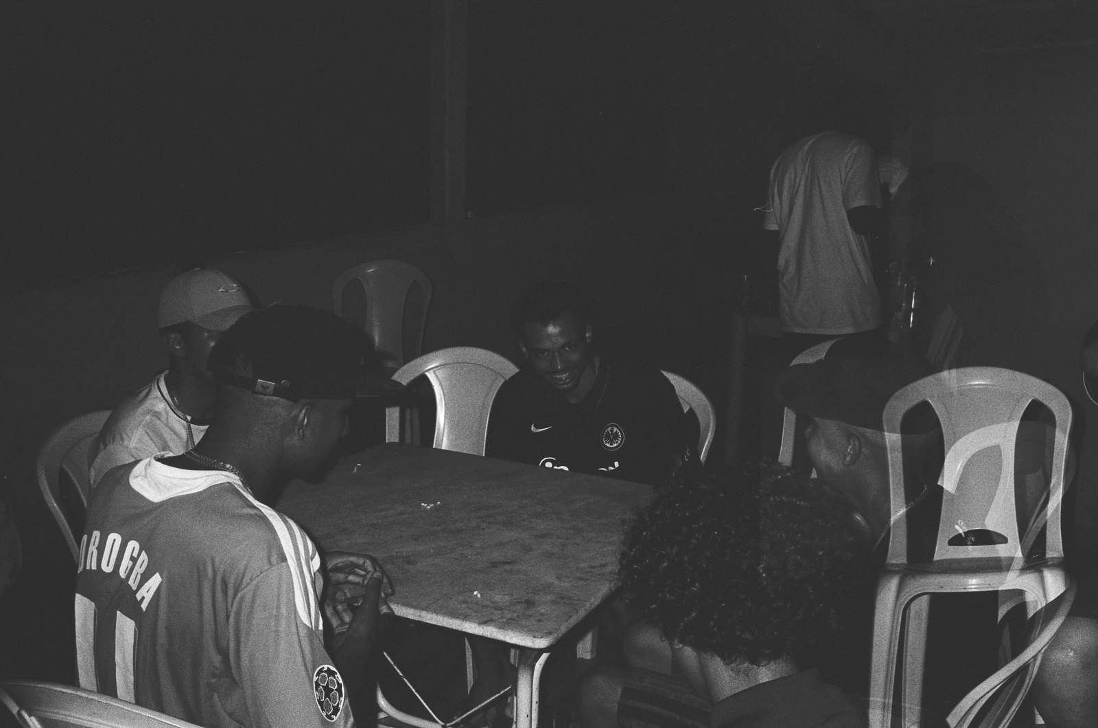 Mesa de bar à noite, homens jogando cartas entre cadeiras de plástico