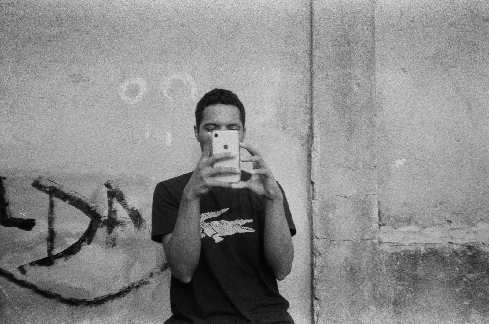 Jovem fotografando com o celular em frente ao muro pichado